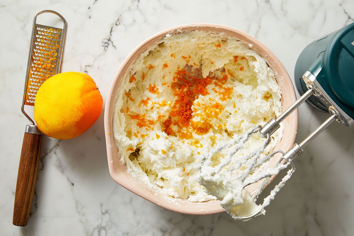Overhead shot of orange zest being mixed into frosting in a small bowl with a whisk.