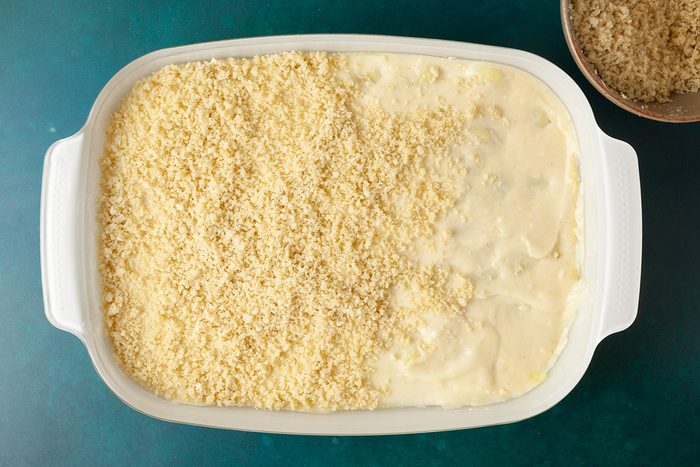 Overhead shot of a white baking dish filled halfway with mac and cheese, with breadcrumbs covering the left side and the creamy macaroni exposed on the right, alongside a small bowl of extra breadcrumbs