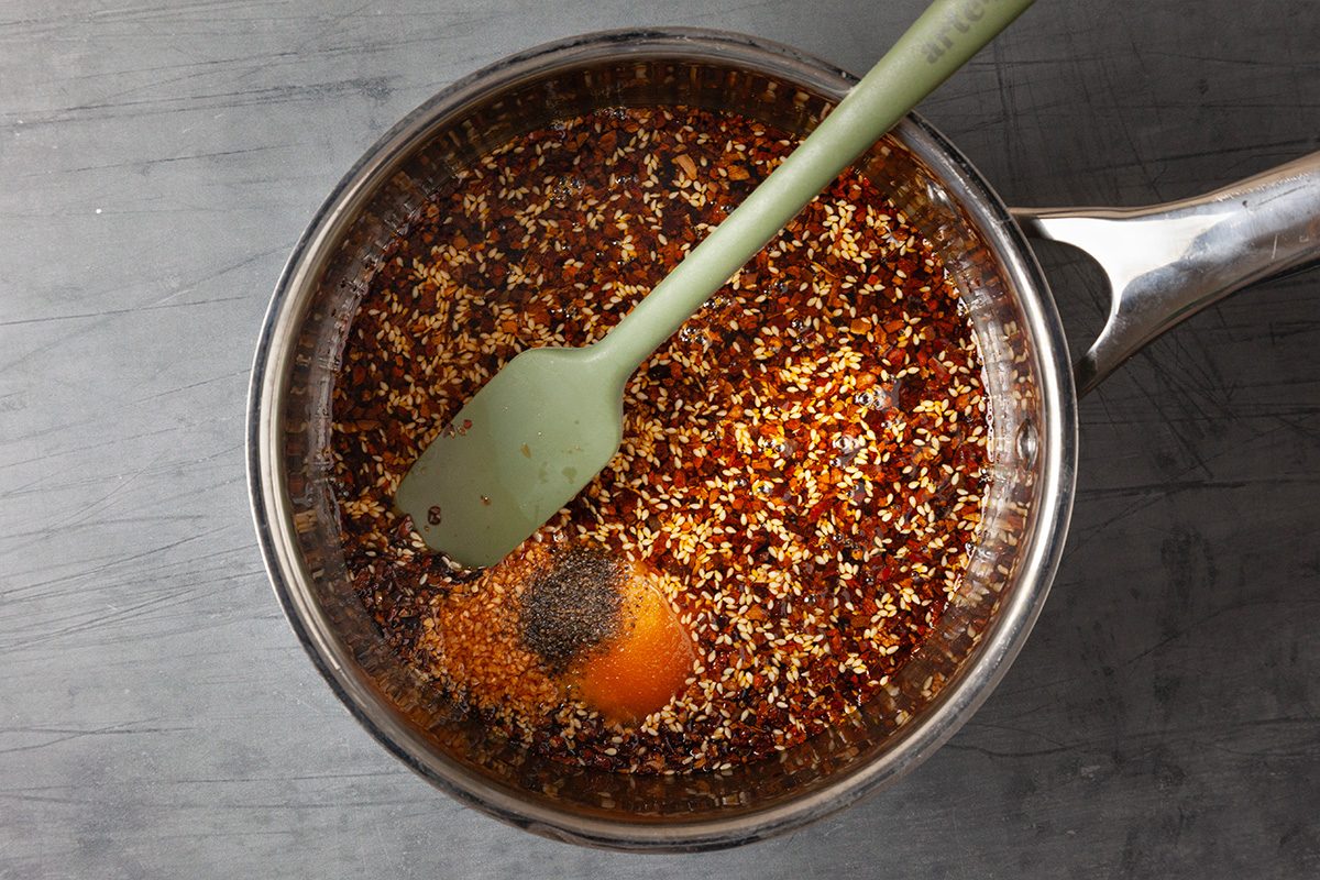 Overhead shot of a saucepan filled with bubbling chili oil as a silicone spatula stirs the mixture.