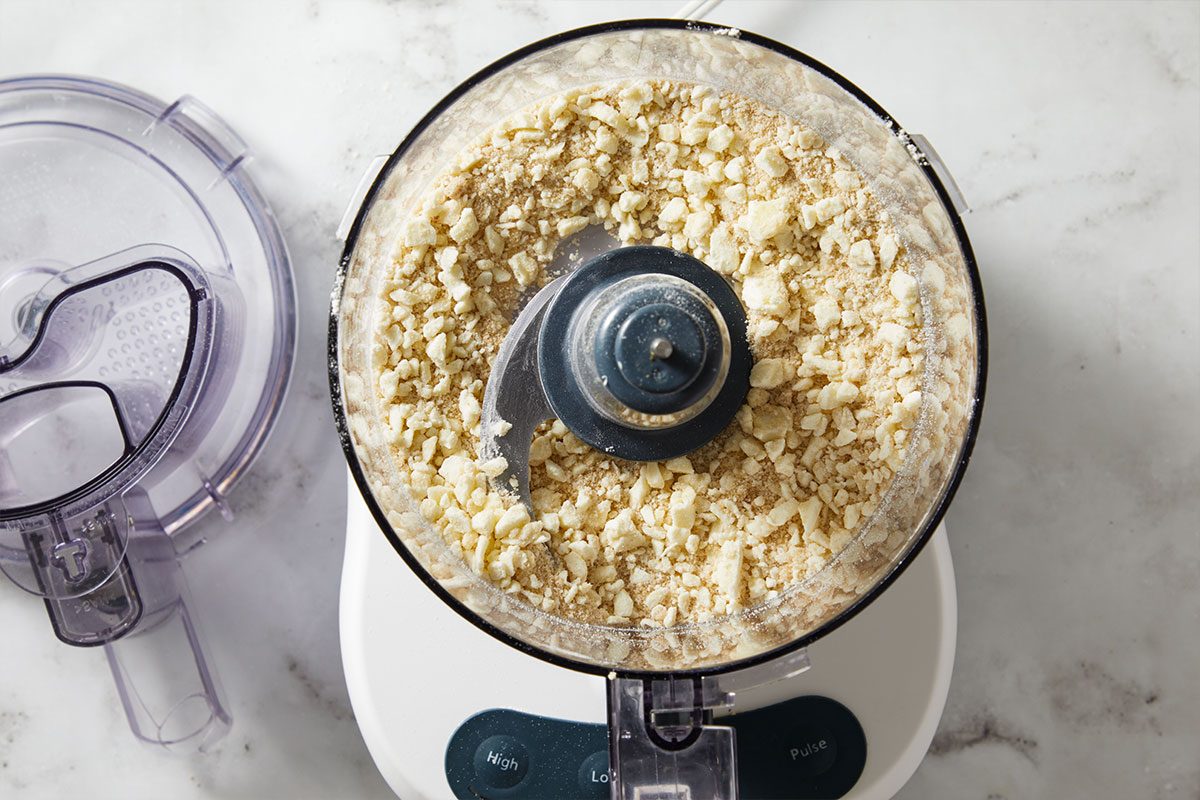 Overhead shot of a food processor filled with finely ground brown sugar on a marble countertop.