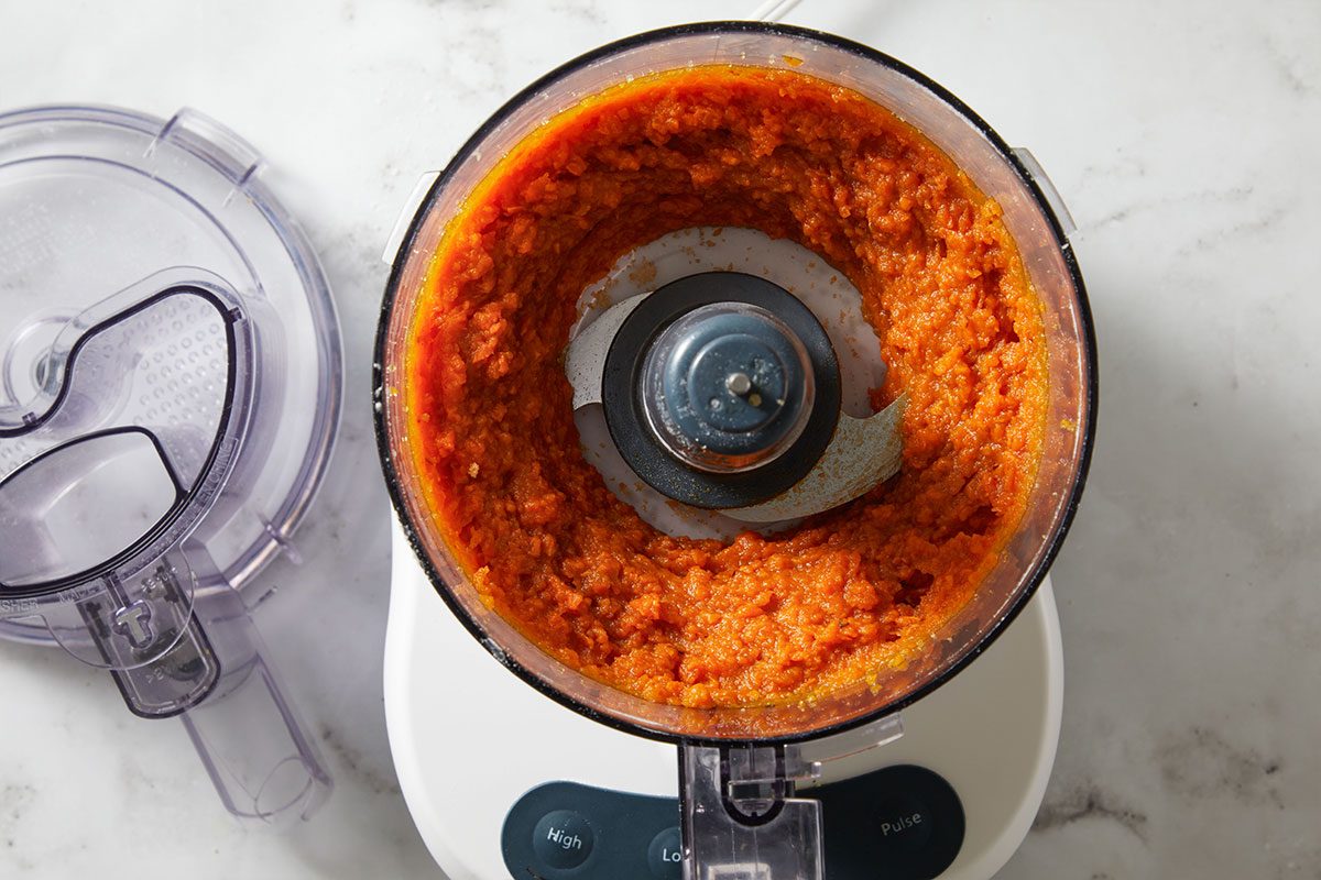 Overhead shot of a food processor filled with pureed sweet potatoes on a marble countertop.