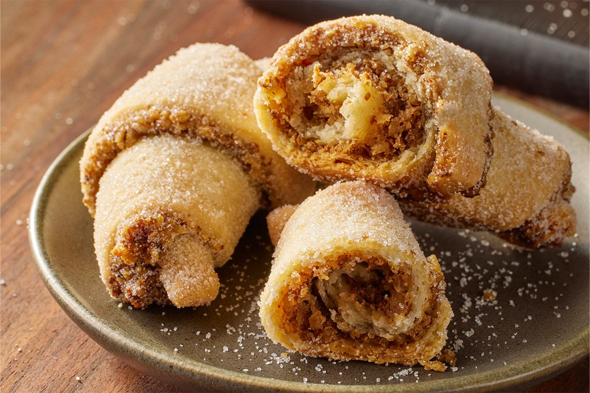 Close-up of three golden-brown, sugar-dusted Horn Walnut Cookies stacked to showcase their flaky texture and crumbly, nutty filling;