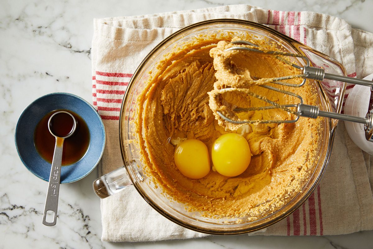 Overhead shot of a mixing bowl filled with peanut butter cookie dough, topped with two cracked eggs