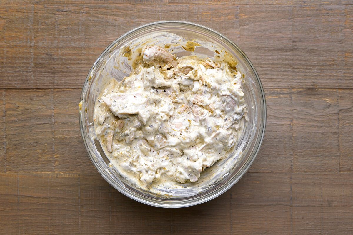 A glass bowl filled with creamy, chunky dip or spread sits on a wooden surface. The dip appears to have a mix of white and light brown ingredients blended together.