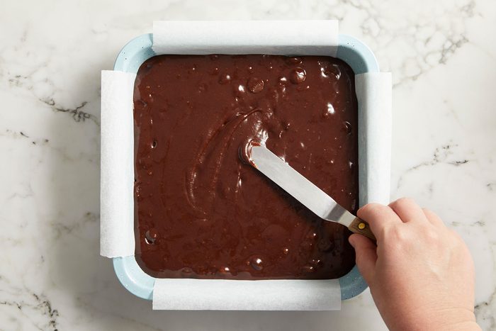 Transfering the brownie batter to the prepared pan and spreading it into an even layer.