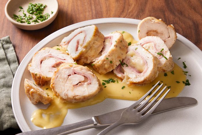 Stuffed Chicken Rolls with garnishing of parsley with some cutlery on a white plate.