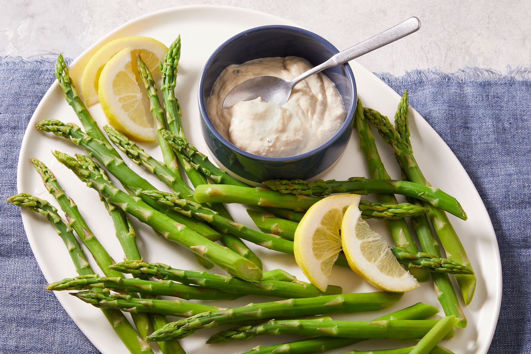 Asparagus With Horseradish Dip in plate and bowl with lemon wedges on side.