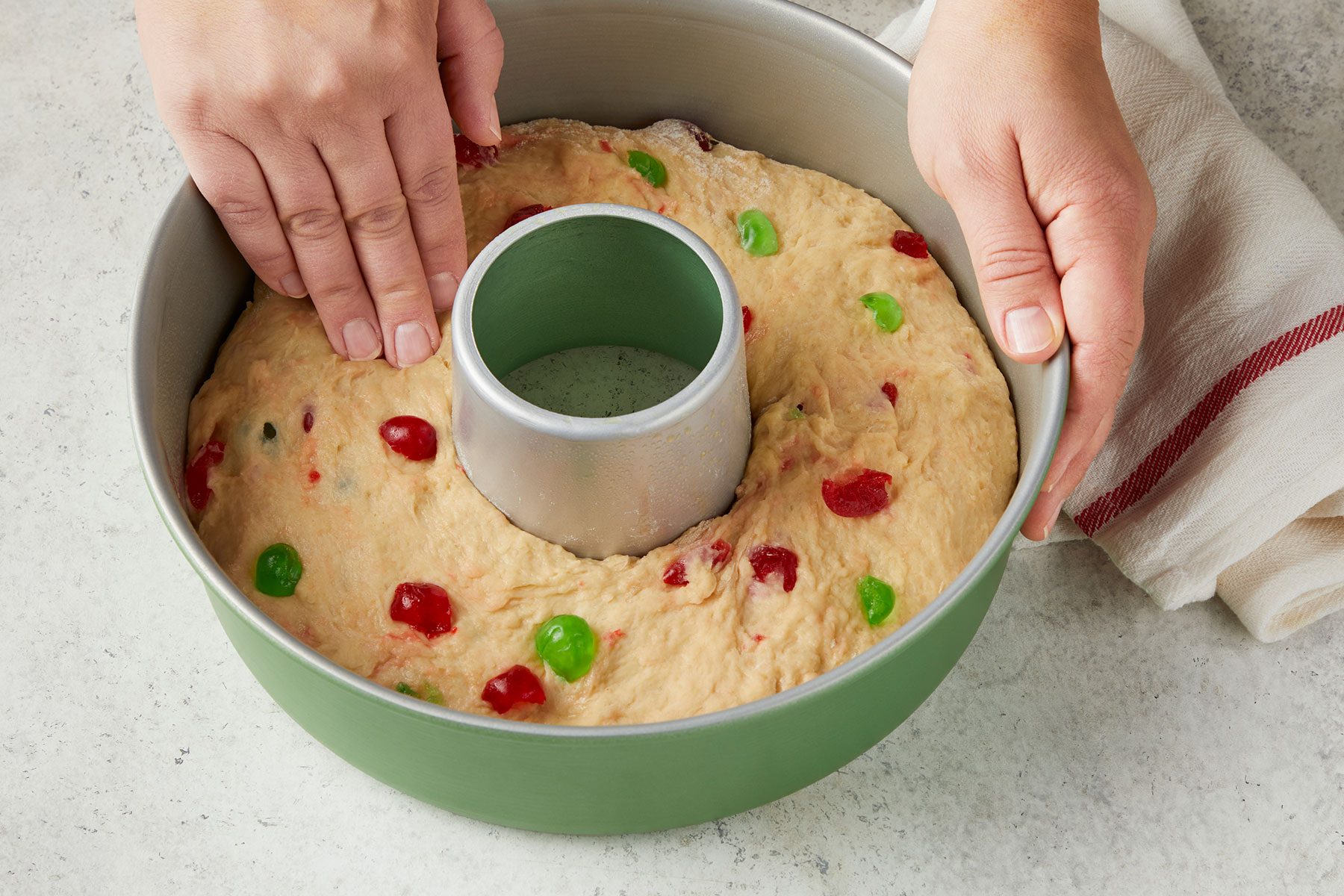 Patting dough evenly into a greased 10-inch tube pan with kitchen towel placed on side.