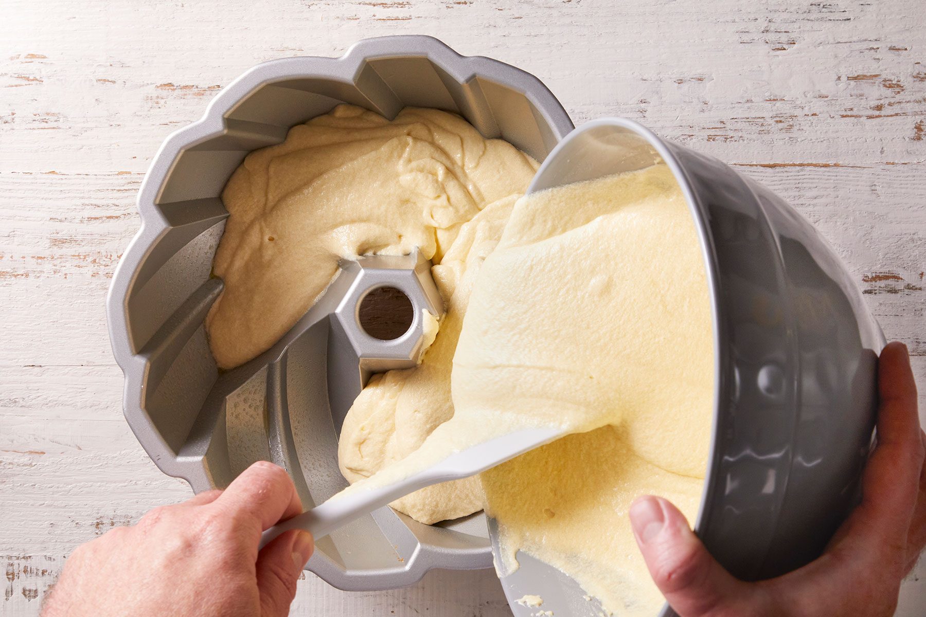 Transferring cake batter to a greased and floured 10-inch fluted tube pan.