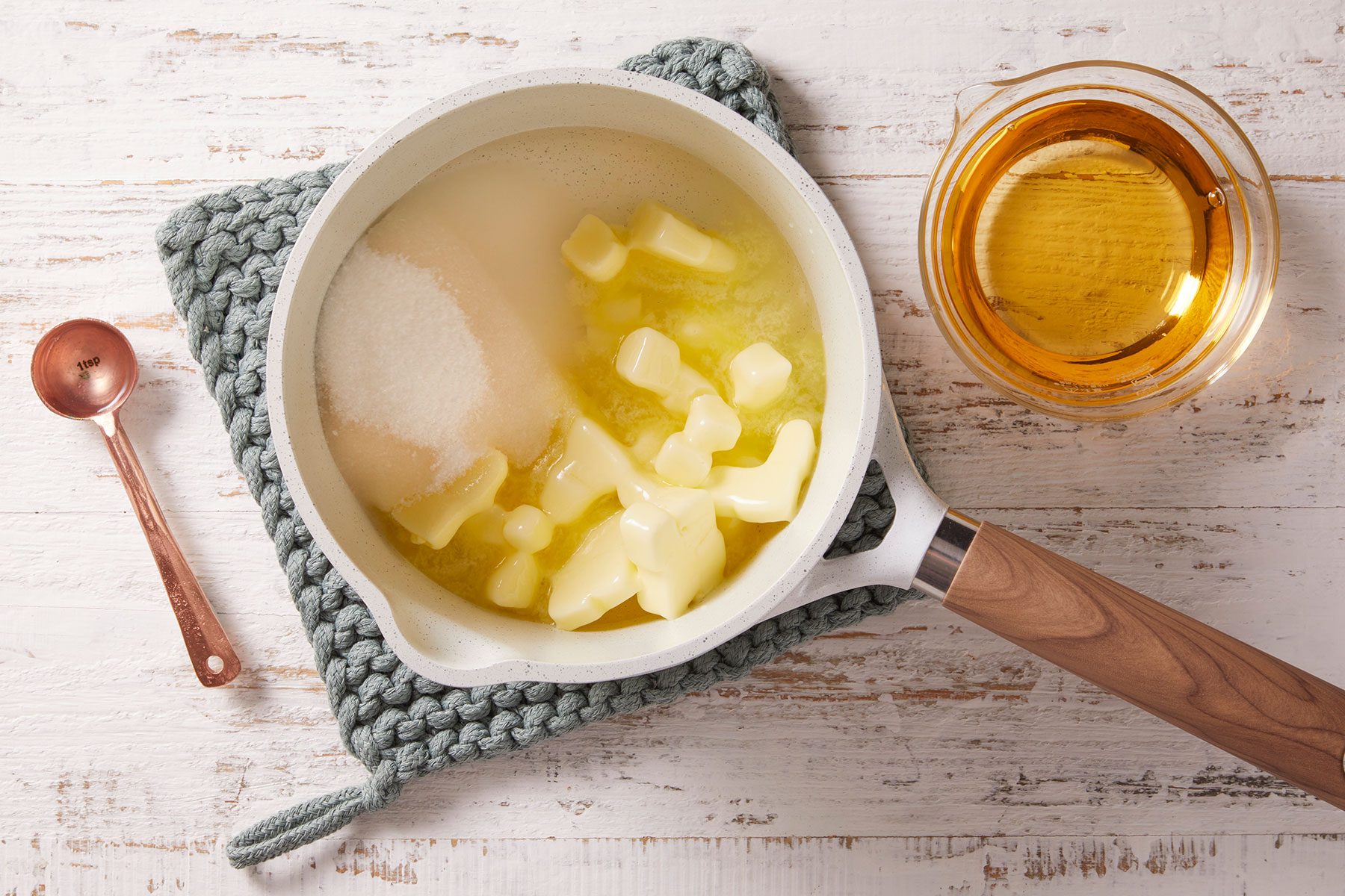 Heated butter, water, sugar and salt in a small saucepan with a spoon and glass of rum kept on side.
