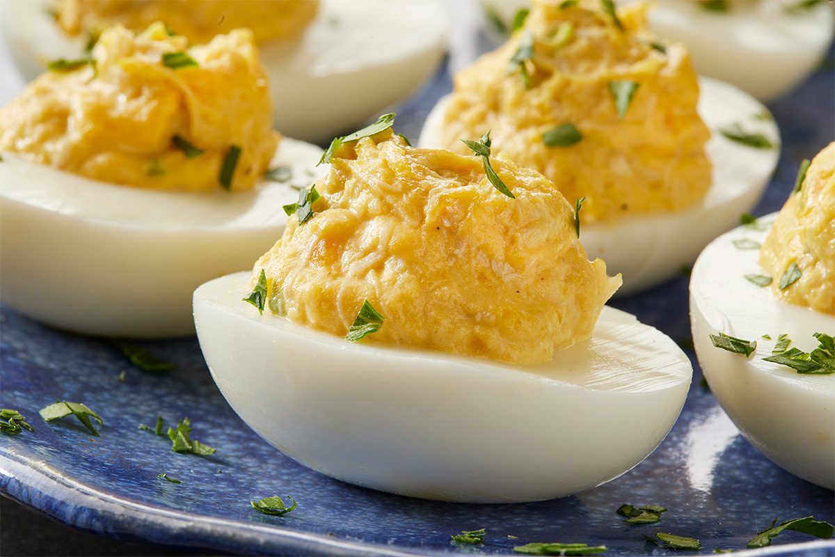 Close-up of deviled eggs on a blue plate. The eggs are halved, filled with a creamy yellow yolk mixture, and garnished with chopped herbs.