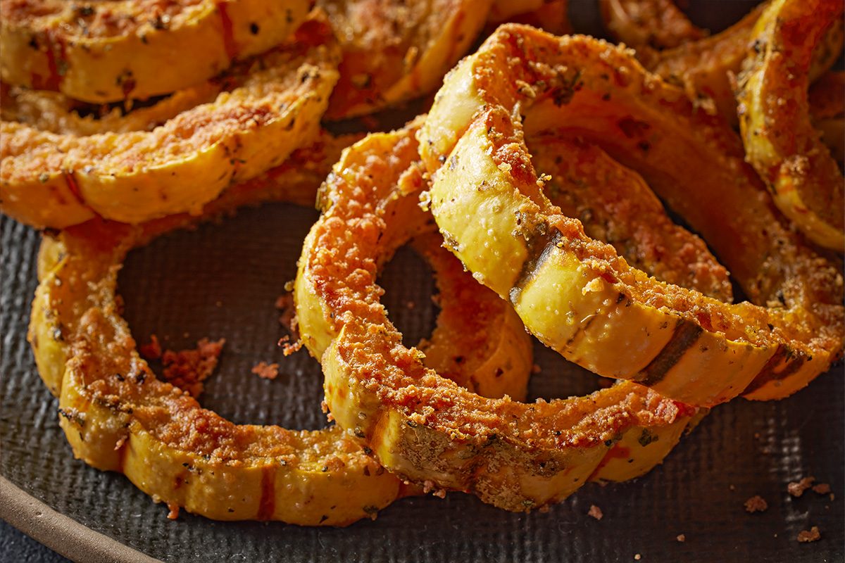 Closeup shot of Crispy Delicata Squash Rings, showing their golden, seasoned coating and tender roasted texture on a dark plate;