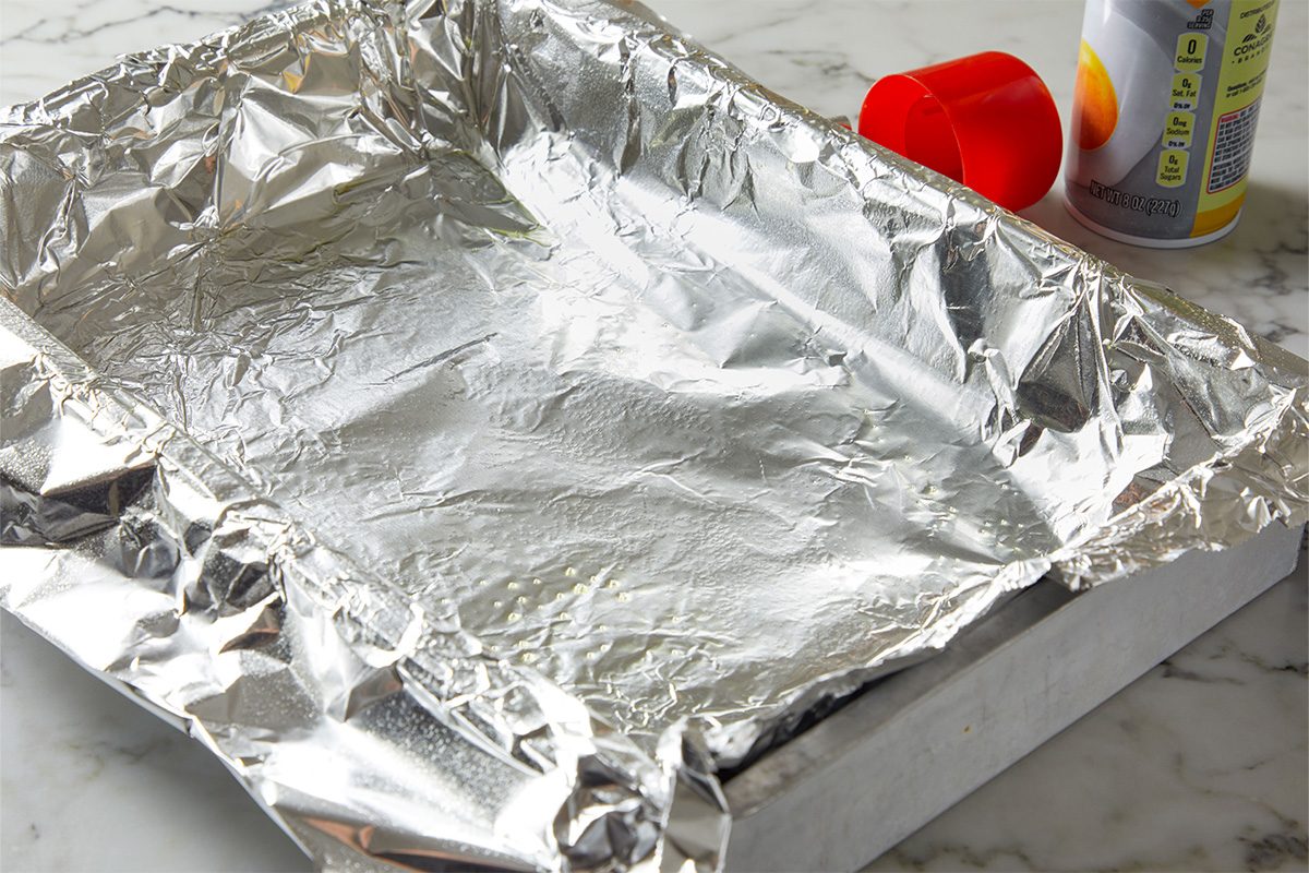 Overhead shot of a foil-lined baking pan being sprayed with nonstick cooking spray, ready for toffee preparation.