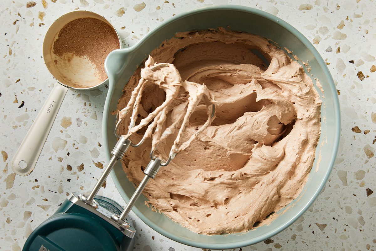 Creamy chocolate frosting being mixed in a bowl with a hand mixer, showing a smooth, light texture.