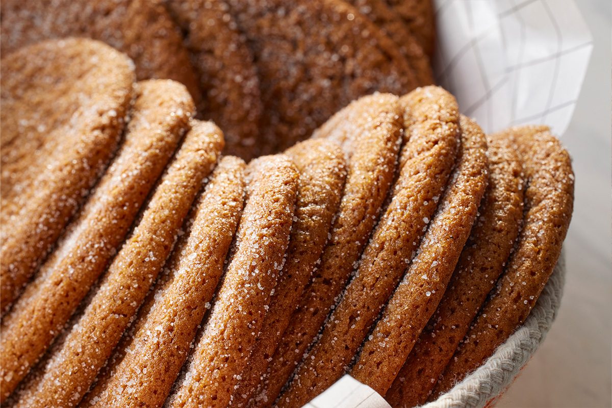 Close-up shot of a stack of round, golden-brown Joe Froggers cookies dusted with sugar, neatly arranged in a basket lined with parchment paper;