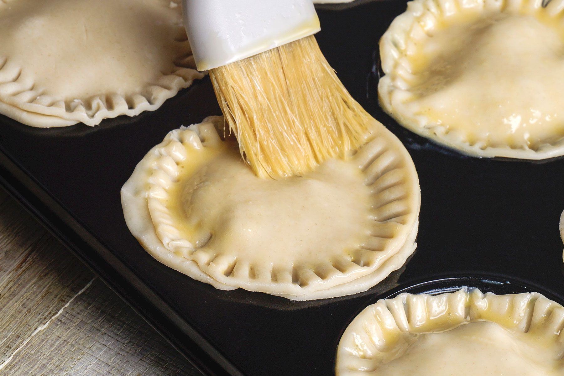 Brushing egg wash over the tops of unbaked Mini Pork Pies.