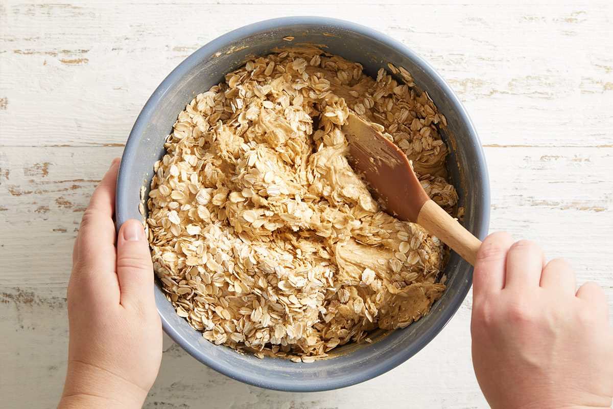 Overhead shot of cookie dough being mixed by hand in a blue bowl, showing thick, textured dough.