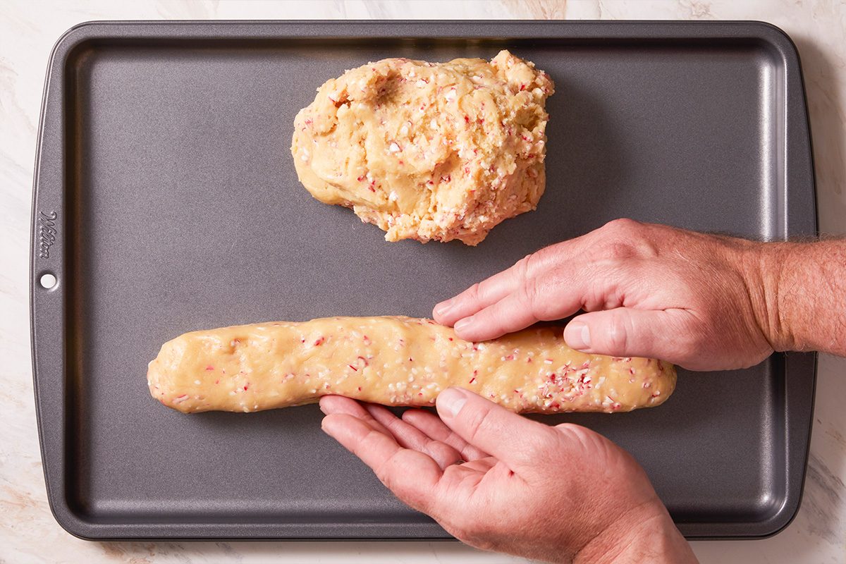 Overhead shot of hands shaping biscotti dough into a log on a baking sheet before baking.