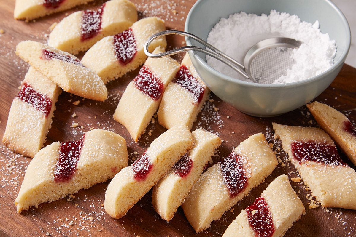 3/4 shot of multiple finished Split-Second Cookies laid out on a wooden board with a small sieve and powdered sugar.