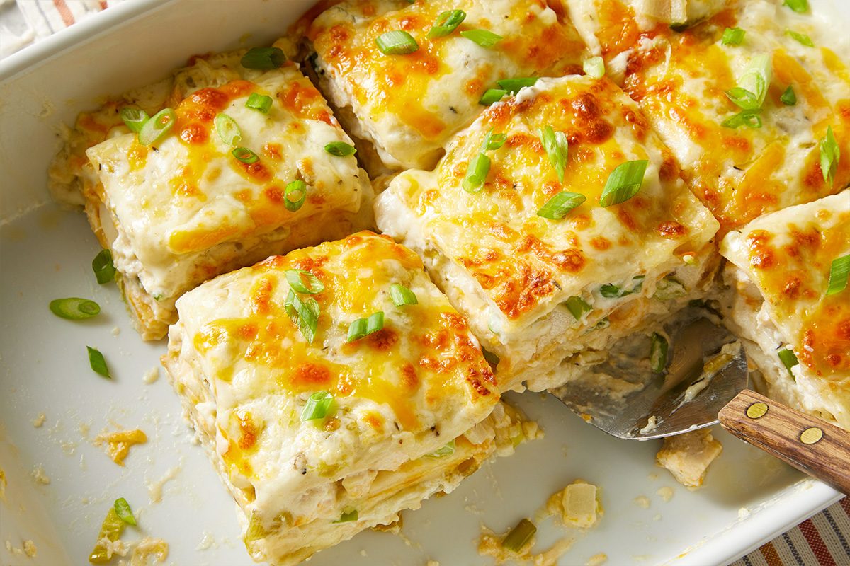 Close overhead view of several cut squares of Chicken Chile Lasagna in the pan, highlighting the golden, bubbly cheese topping and the layered interior.