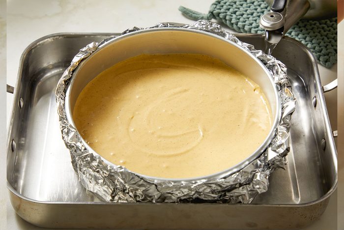 Overhead shot of the filled springform pan placed inside a roasting pan, ready for the water bath baking method.