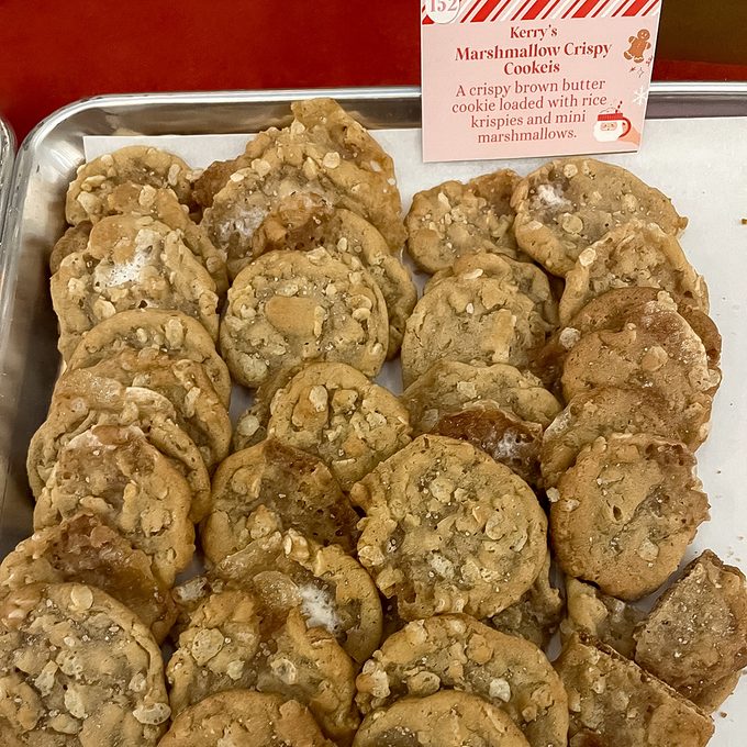 A tray of round, golden-brown cookies labeled “Kerry’s Marshmallow Crispy Cookies,” featuring a crispy texture with visible bits of rice krispies and mini marshmallows sprinkled on top.